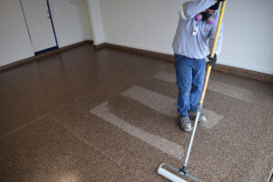 Expert installer applying a clear 100%-solids polyaspartic top coat to a garage floor.