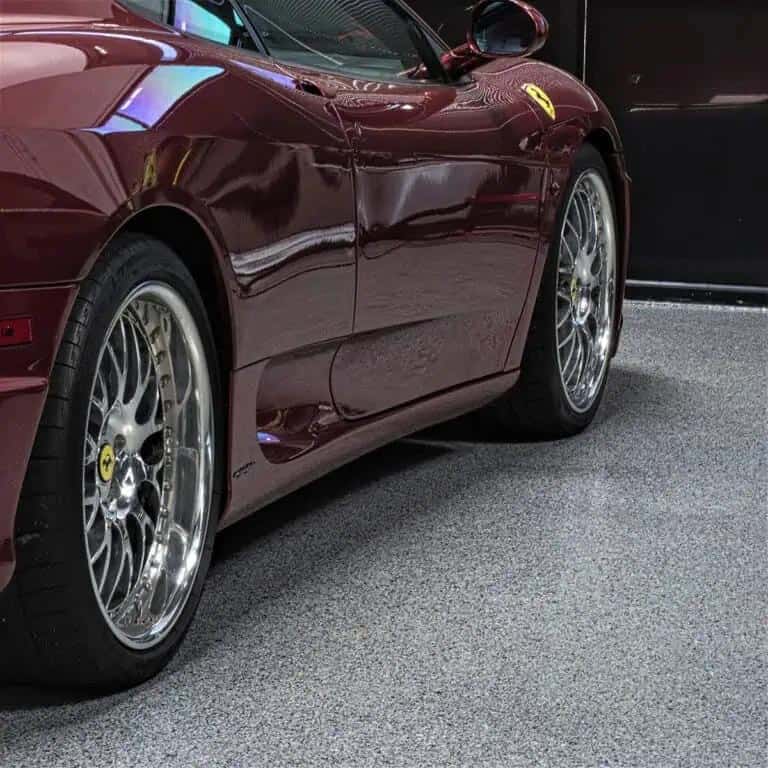 Red sports car atop a gray, full flake mica-infused epoxy polyaspartic garage floor coating. 